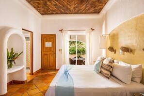 A hotel room with a bed, a wooden door, a window with curtains, a small table with chairs, and a potted plant. - Casa Real Sayulita Hotel Boutique (Sayulita)