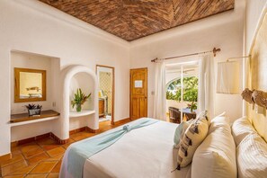 Un dormitorio con una cama grande, una puerta de madera, una mesita con una silla y una ventana con cortinas.