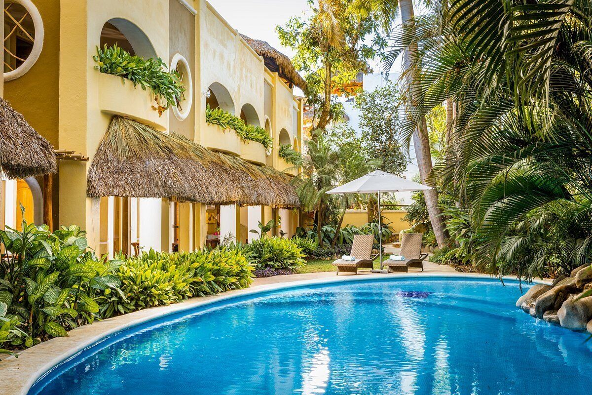 A pool area with a thatched-roof building, lounge chairs, and tropical plants.