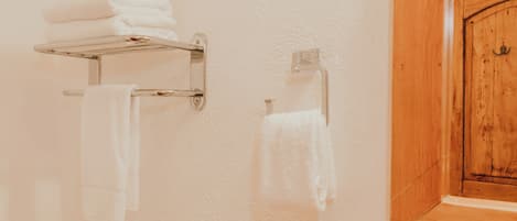 Un baño con un perchero con toallas dobladas, un dispensador de papel higiénico y una puerta de madera.