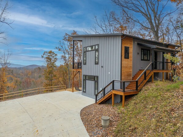 Eine moderne Holzhütte mit einer Terrasse, Holzstufen und Blick auf den umliegenden Wald.