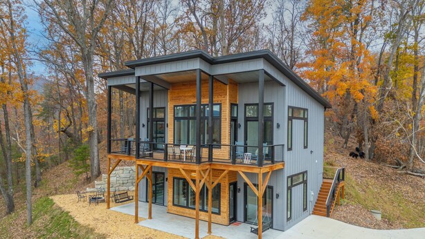 A modern two-story cabin with a balcony, large windows, and a stone foundation. - Modern Mountain Mansion with stunning view (Lake Lure)