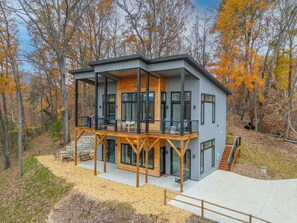 Eine moderne, zweistöckige Holzhütte mit Balkon, großen Fenstern und einem Steinfundament.
