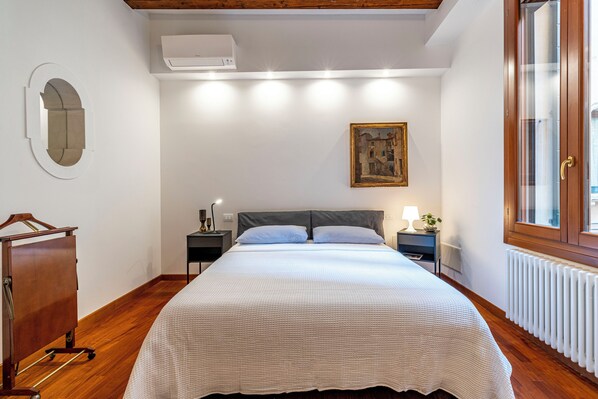 Una camera da letto con un letto, un comodino, una cassettiera, una finestra e un quadro appeso al muro.