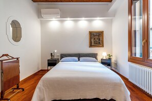 Ein Schlafzimmer mit Bett, Nachttisch, Kommode, Fenster und einem Gemälde an der Wand.