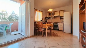 A compact kitchen with a dining area, a refrigerator, and a sliding glass door leading to a balcony with chairs. - Ground floor Apartment Tihana with washing machine for up to 4 Guests (Krk)