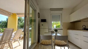 A compact kitchen with a dining area, a refrigerator, and a window with blinds.