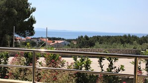 A balcony with a metal railing overlooking a coastal area with houses and trees.