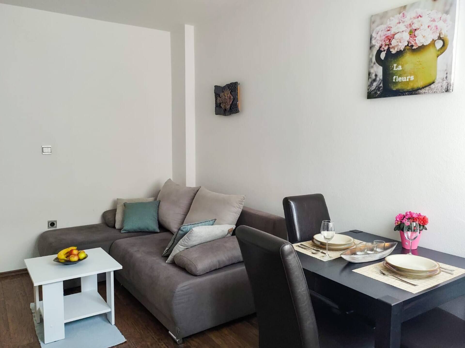 Een moderne woonkamer met een grijze bank, een klein wit bijzettafeltje en een eettafel gedekt voor twee personen.