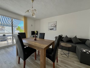 Ein Essbereich mit Holztisch und Stühlen, einer Couch, einem kleinen runden Tisch und einem Fernseher im Hintergrund.