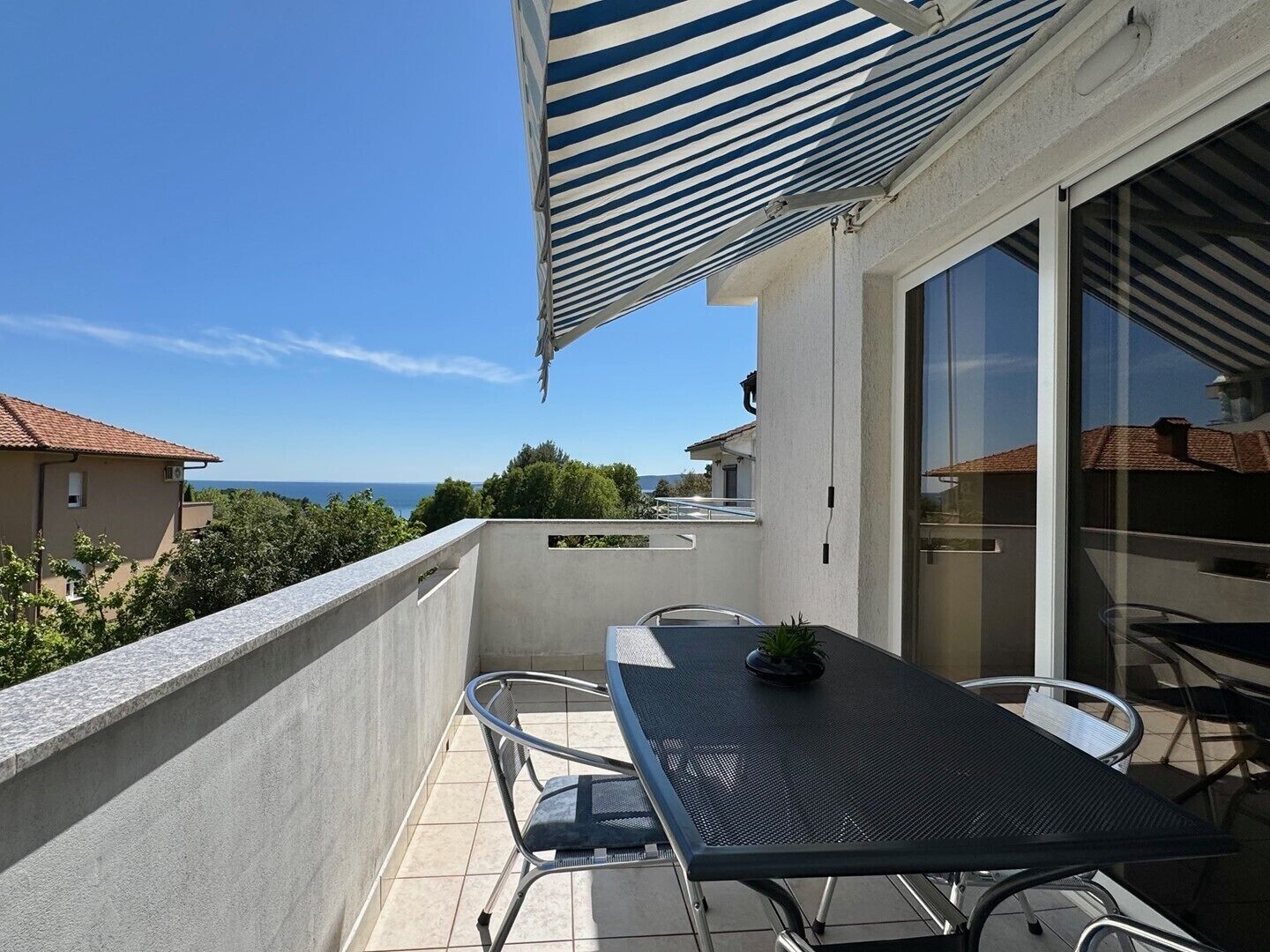 A balcony with a table and chairs, a striped awning, and a view of the sea.