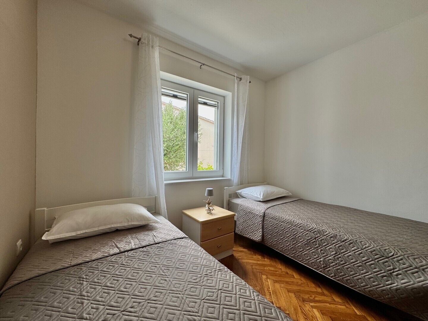 A bedroom with two beds, a window, a bedside table, and a nightstand.