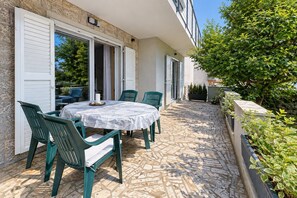 An outdoor patio with a round table and chairs, a door leading to a covered area, and a stone-tiled floor.