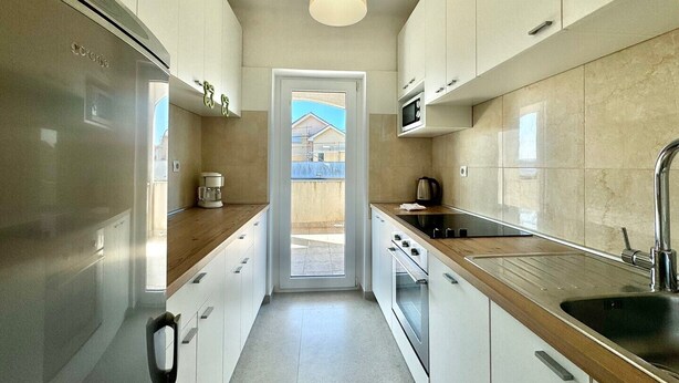 A modern kitchen with white cabinets, a stainless steel refrigerator, a microwave, a coffee maker, and a view of the outside.