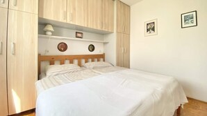 A bedroom with a bed, wooden wardrobe, and a shelf with a lamp and decorative items.