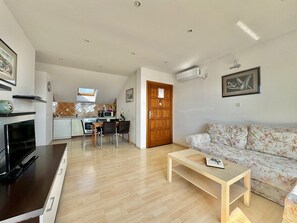 Un salon moderne avec un canapé, une table basse, un téléviseur et une cuisine en arrière-plan.