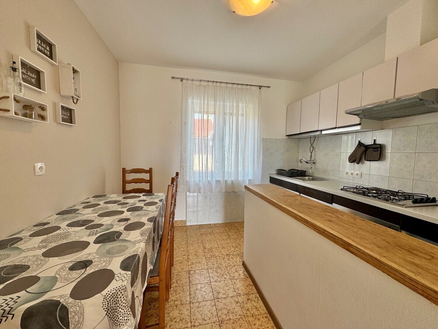 Cocina compacta con comedor, estufa y ventana con cortinas translúcidas.