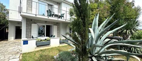 A modern two-story building with a balcony, outdoor seating, and a garden with large agave plants.