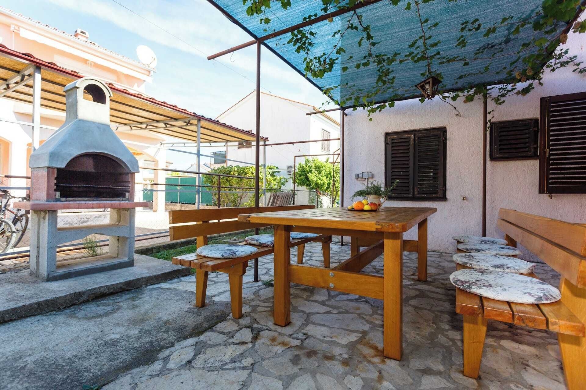 Un patio al aire libre con suelo de piedra, una mesa de madera, bancos y un horno de pizza.