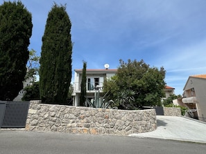 A two-story building with a stone wall in the foreground, a balcony with chairs, and a clear blue sky.