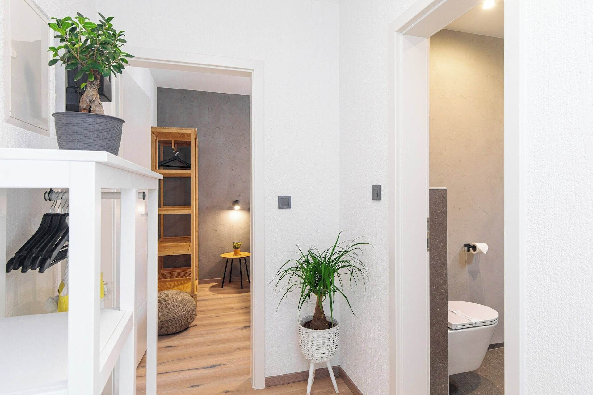 A hallway with a white wardrobe, a potted plant, a wooden bench, and a bathroom with a toilet.