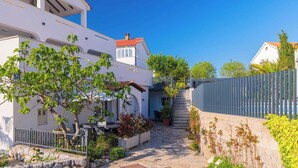 A narrow stone pathway leading to a white building with a red-tiled roof, surrounded by greenery and a metal fence. - Spacious Ground floor Apartment LiJan °1 with Two Bedrooms (Krk)