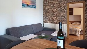 Una habitación acogedora con pared de piedra, un sofá gris, una mesa de madera con una botella de vino y una cama al fondo.