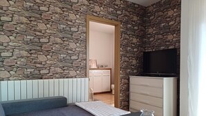 Un cuarto acogedor con pared de piedra, un sofá gris, una mesita con un florero de vidrio y un televisor sobre un mueble.