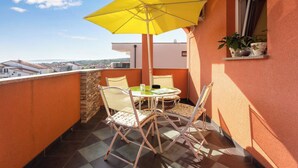 Ein kleiner Balkon mit einem gelben Sonnenschirm, zwei Stühlen, einem Tisch und einem Fenster mit Topfpflanzen.