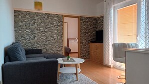 Ein modernes Wohnzimmer mit einer Wand aus Stein, einem grauen Sofa, einem runden Couchtisch und einem Essbereich mit einem weißen Stuhl und einem Schrank.