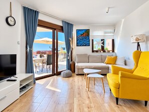 A modern living room with a sofa, yellow armchair, TV, and a dining area with outdoor seating. - Holiday Home Ira with Pool and BBQ, Family Friendly, WiFi, Parking, Pets Allowed (Krk)