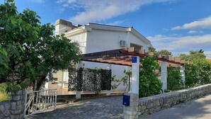 A building with a pergola entrance, stone walls, and a garden with trees and a hedge. - Charming Apartment Luka Near Ježevac Beach with Terrace (Krk)