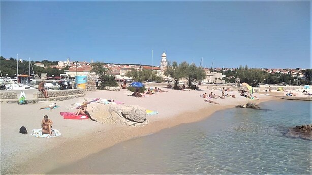 A beach with clear water, people sunbathing, and a historic building in the background. - Charming Apartment Luka Near Ježevac Beach with Terrace (Krk)