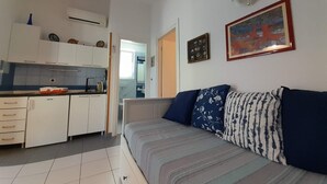 A compact living space with a kitchenette, a sofa with patterned cushions, and a framed picture on the wall. - Charming Apartment Luka Near Ježevac Beach with Terrace (Krk)