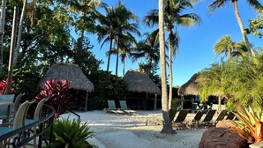 Un resort frente a la playa con construcciones de techo de paja, sillas de descanso y palmeras.