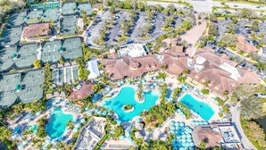 Vista aérea de un complejo turístico con varias piscinas, canchas de tenis y un estacionamiento.
