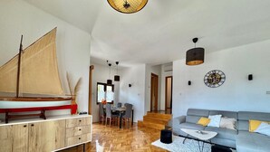 A spacious living area with a wooden herringbone floor, a grey sofa with yellow cushions, a wooden coffee table, and a sailboat model on a wooden cabinet. - Apartment KrisTina with pool, family friendly, WiFi, parking, pets allowed (Krk)