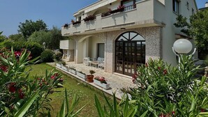 A two-story building with a balcony, a covered patio, and a garden area with potted plants and flowers. - Apartment KrisTina with pool, family friendly, WiFi, parking, pets allowed (Krk)