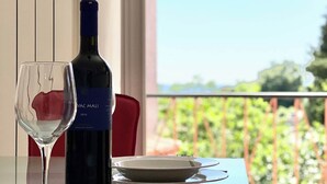 Un tavolo da pranzo con una bottiglia di vino e un bicchiere, affacciato su un balcone con vista sul verde.