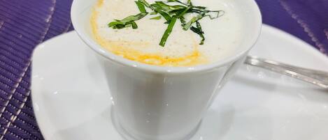 A white cup of soup with green garnish on a white saucer, placed on a purple woven mat.
