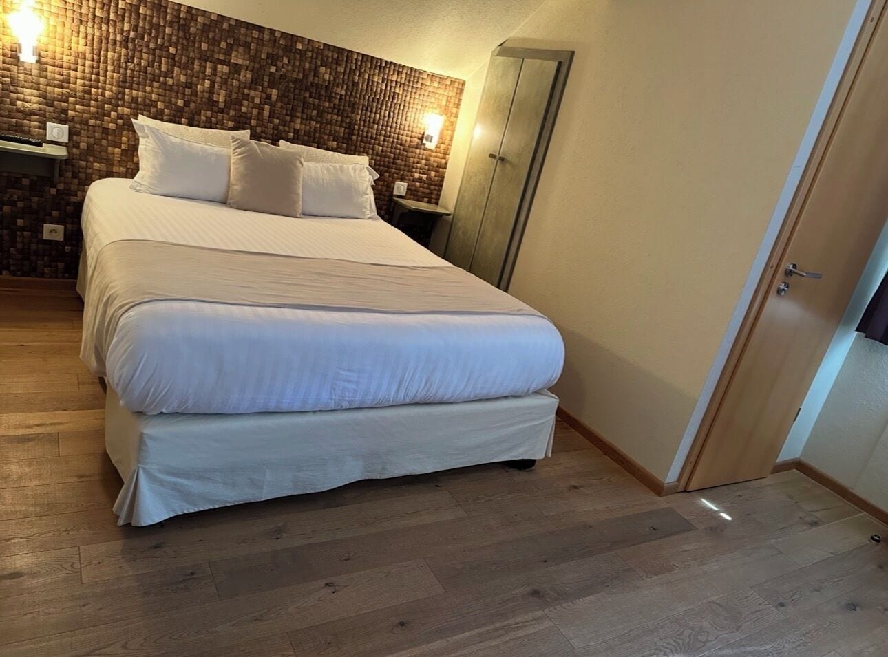 A bedroom with a bed, wooden floor, and a brick-patterned wall.
