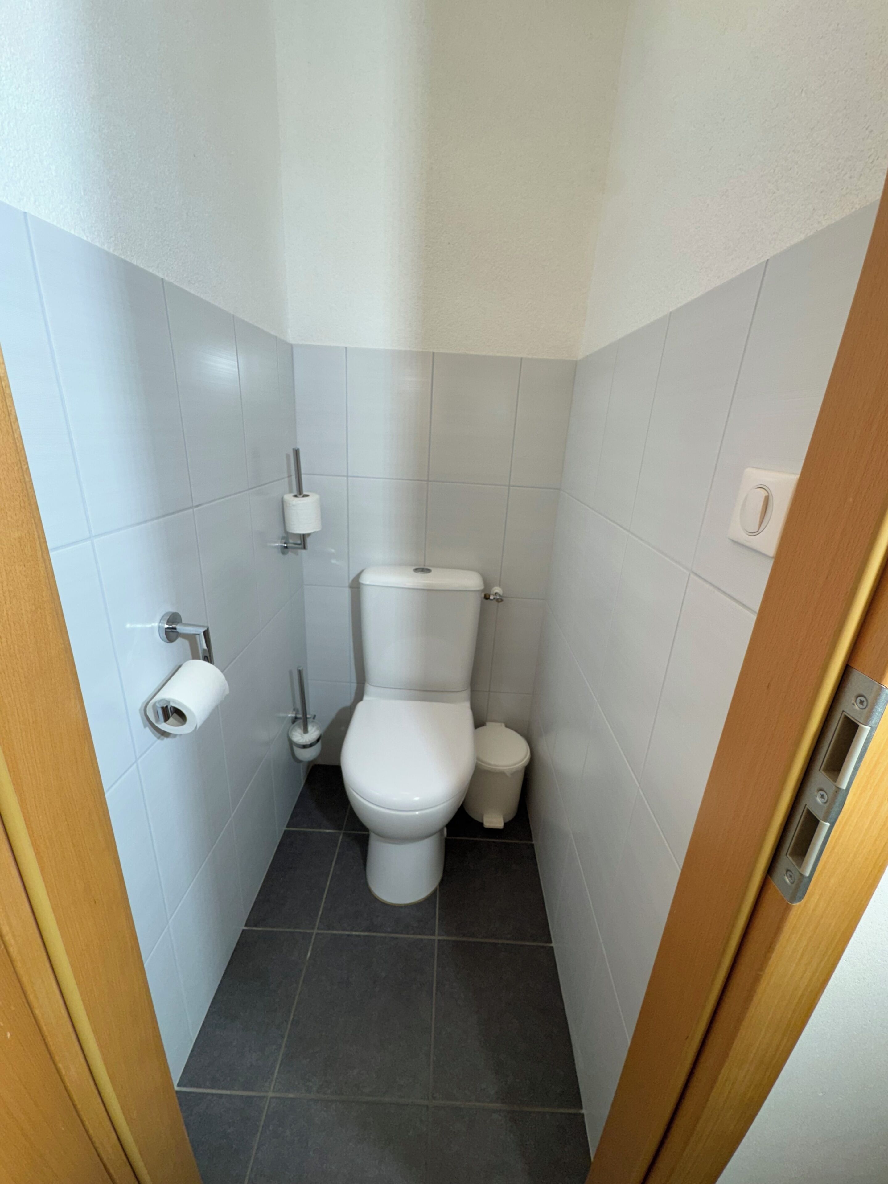 Un baño pequeño y limpio con inodoro, dispensador de papel higiénico, bidé y cubo de basura.