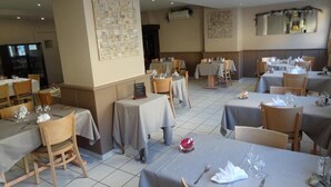 Un restaurant avec de nombreuses tables, chacune mise avec des couverts et des serviettes, et un sol carrelé.