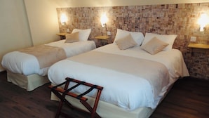 Une chambre d’hôtel avec deux lits, un banc en bois et un mur décoré d’un motif en briques.