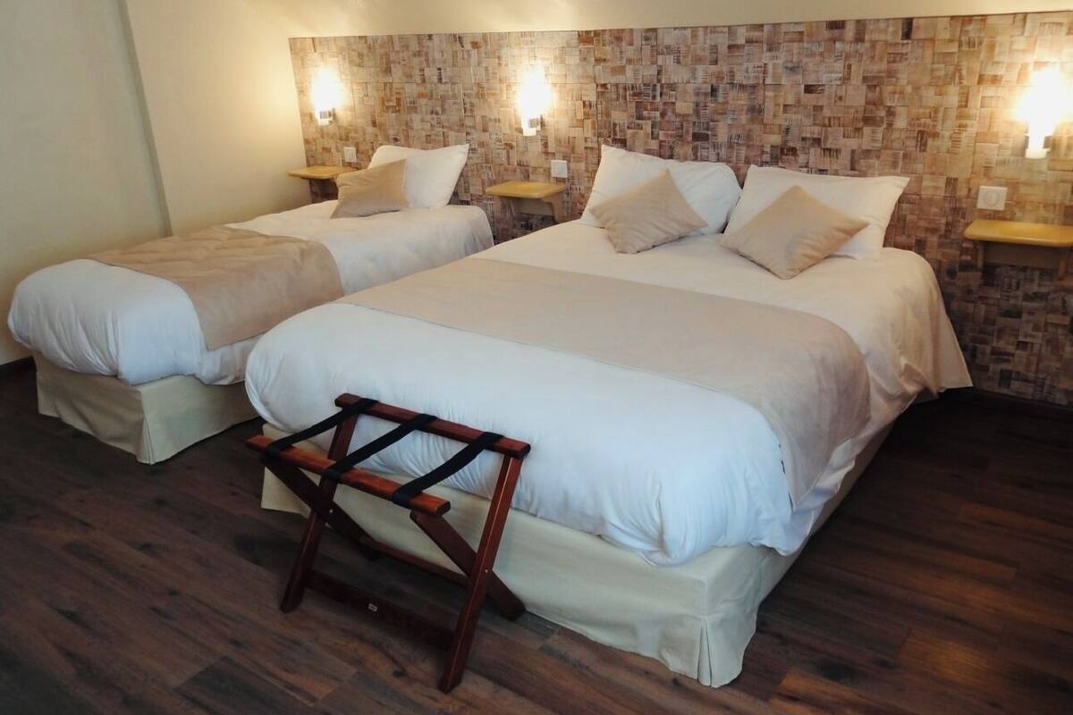 Ein Hotelzimmer mit zwei Betten, einer Holzbank und einer Wand mit Ziegelmuster.