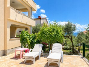A terrace with two white lounge chairs, a pink table, and a small garden area with trees and plants. - Family-friendly apartment Lilly with garden barbecue and trampoline (Krk)