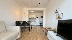 Ett modernt vardagsrum med en vit soffa, en tv och en matplats med ett bord och stolar.