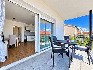 A balcony with a table and chairs, a sliding glass door leading to a kitchen, and a view of the neighborhood. - Apartment Goldie 2° in town Krk with sea view, close to the center, Air conditioning and Wi-Fi (Krk)