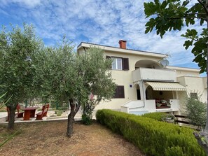 A two-story building with a balcony, a satellite dish, and a small garden area with a table and chairs. - Studio Xenia in Krk in a quiet location with air conditioning and WiFi (Krk)