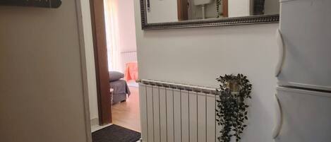 Ein Flur mit Heizkörper, Spiegel und Kühlschrank.